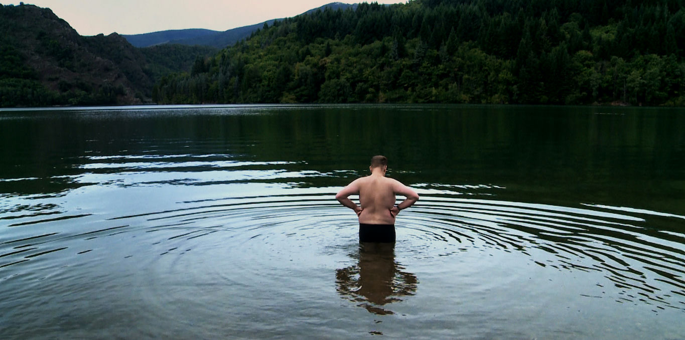 homme en maillot de bain debout de dos au milieu d'un lac