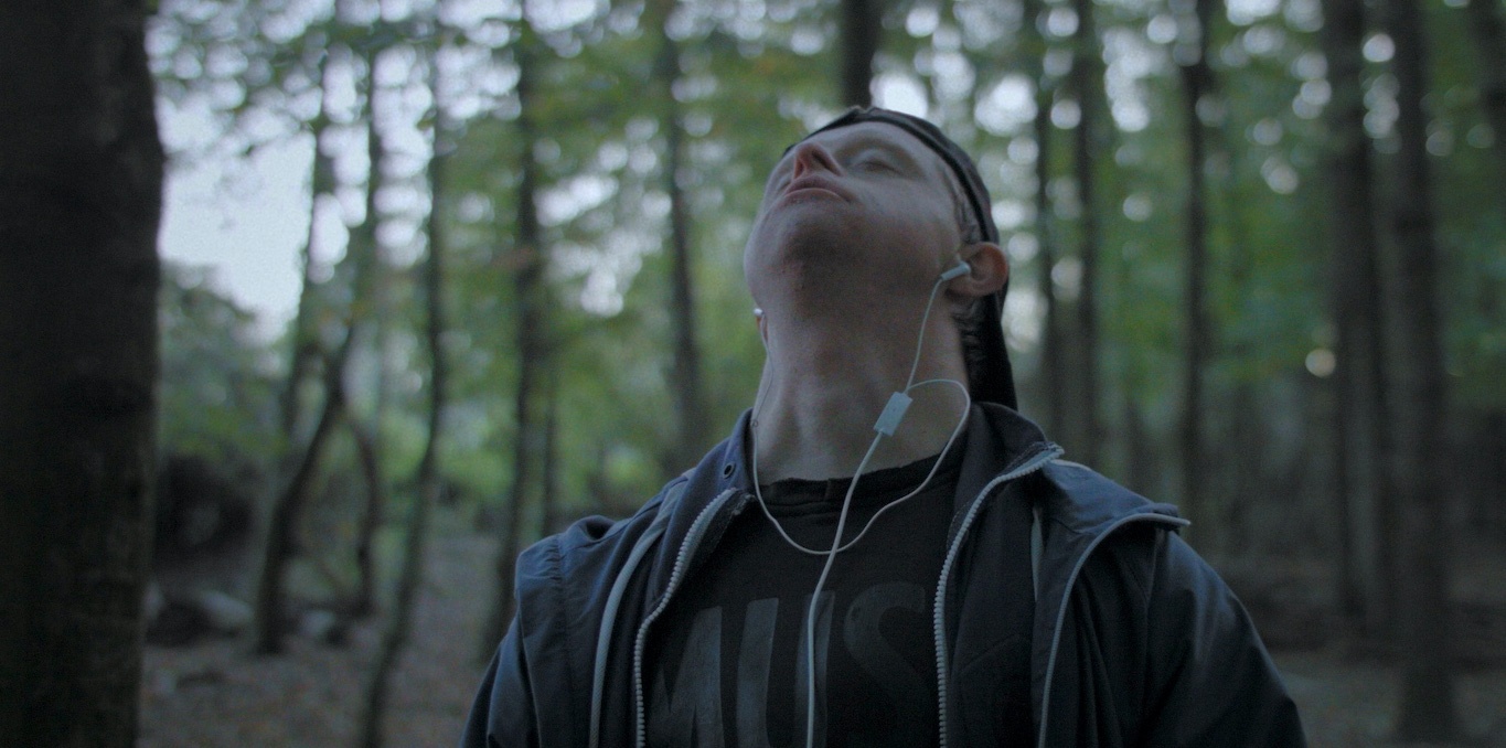 Photo d'un jeune écoutant de la musique la tête renversée en arrière au milieu de la forêt