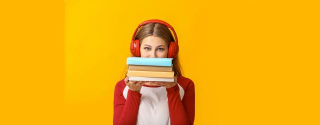 Jeune femme portant un casque audio rouge et tenant trois livres dans ses mains devant son visage