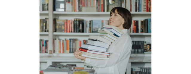 femme portant une pile de livres devant des rayonnages de bibliothèque