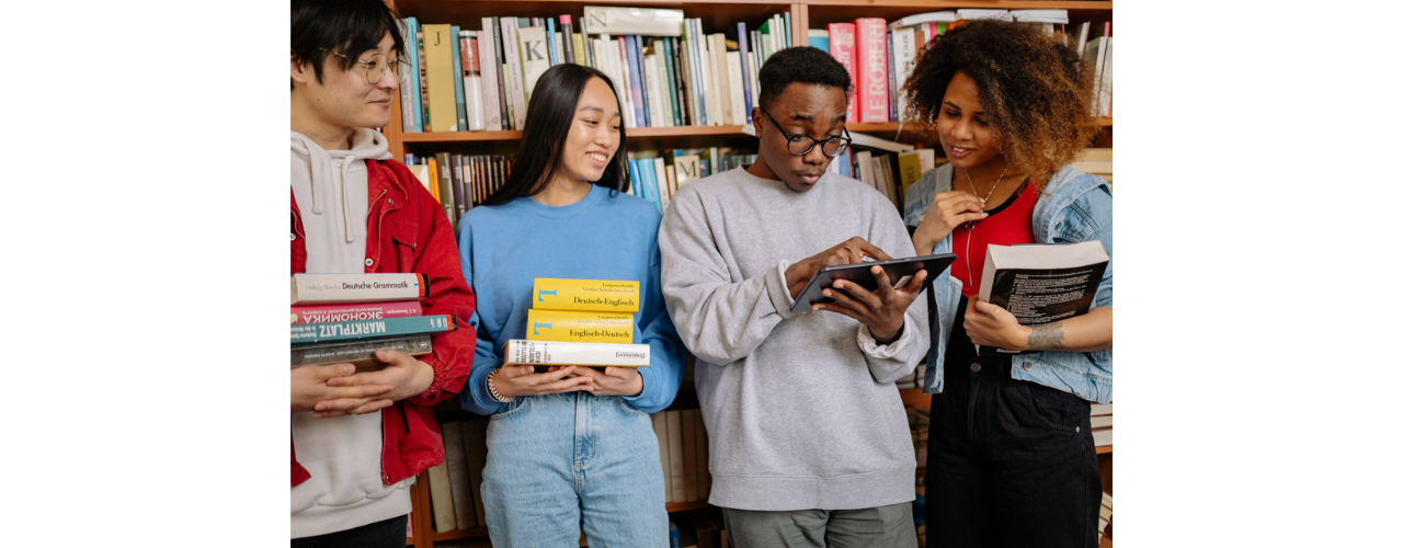 groupe de jeunes devant une étagère, portant des livres et une tablette