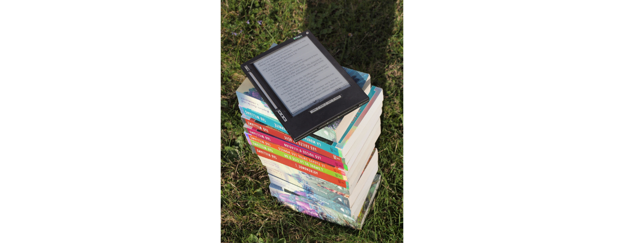 pile de livres posés sur l'herbe avec une liseuse posée sur le dessus