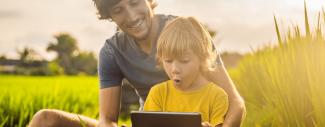 Un papa et son fils regarde une tablette ensemble assis dans un champ